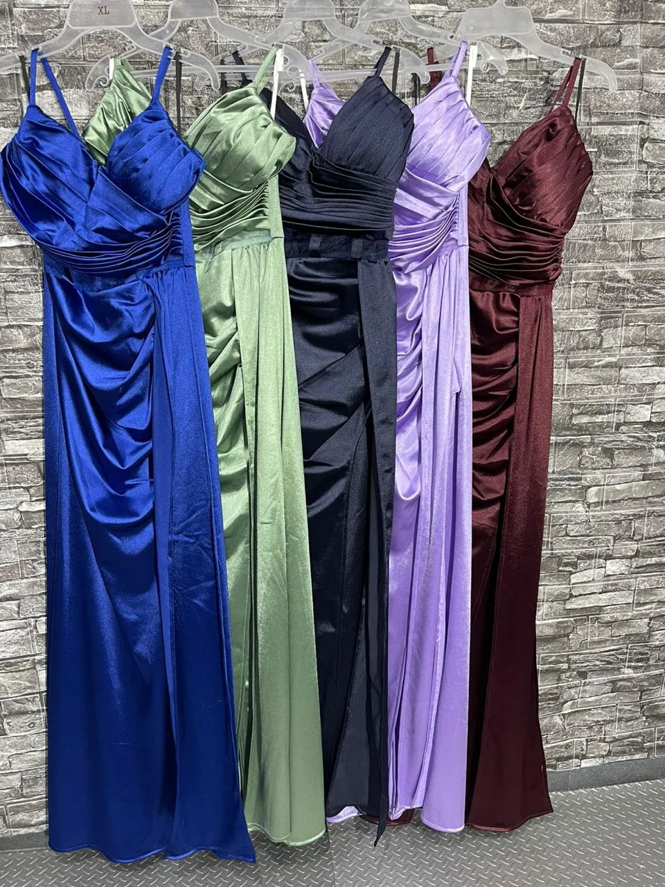 Stock Mayorista Vestidos de Fiesta Patrizze | Envío Directo Mixcalco Variedad de vestidos largos de fiesta en azul rey, verde olivo, marino, lila y tinto, colgados en rack para venta al por mayor por el distribuidor Patrizze.